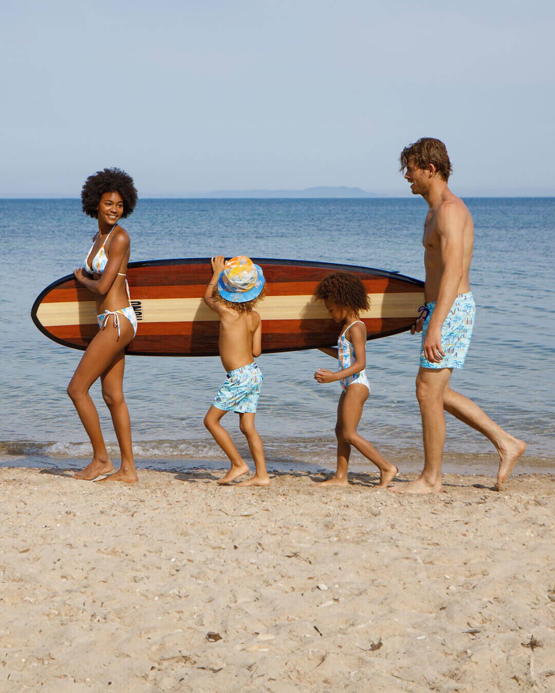 A woman, a child, and a man holding a surfboard on the beach. 